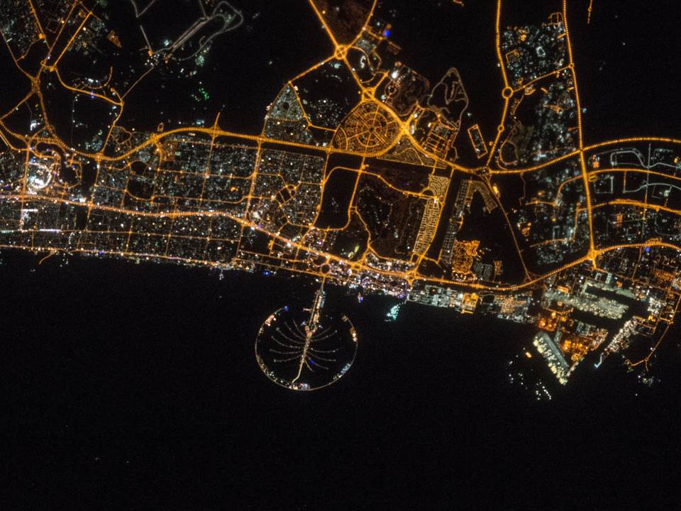 Dubai at night from space, with Palm Jumeirah lit in the sea below the coast road