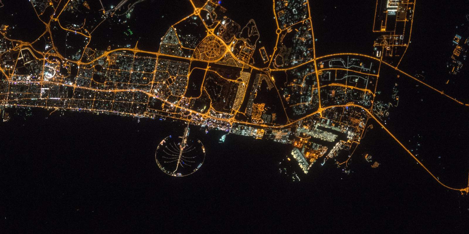 دبي ليلاً من الفضاء ونخلة جميرا مضيئة في البحر أسفل الطريق الساحلي