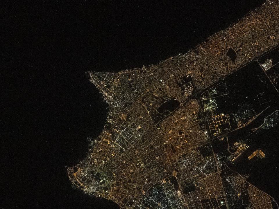 Kuwait City at night from space, its streets in amber light along the dark water of the bay
