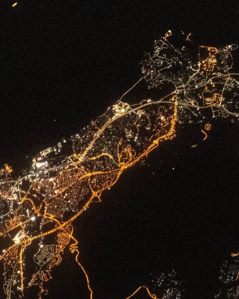 مسقط والسيب ليلاً من الفضاء والطريق الساحلي والمطار بأضواء كهرمانية بجوار بحر داكن