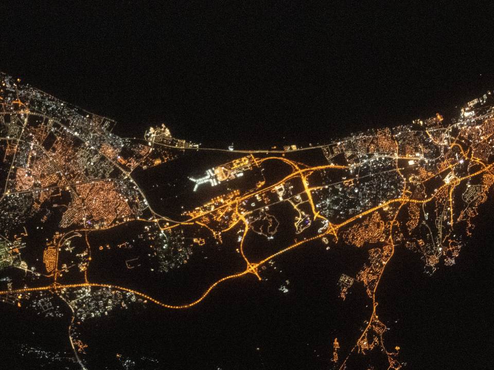 Muscat and Al Seeb at night from space, the coast road and the airport in amber light beside a dark sea